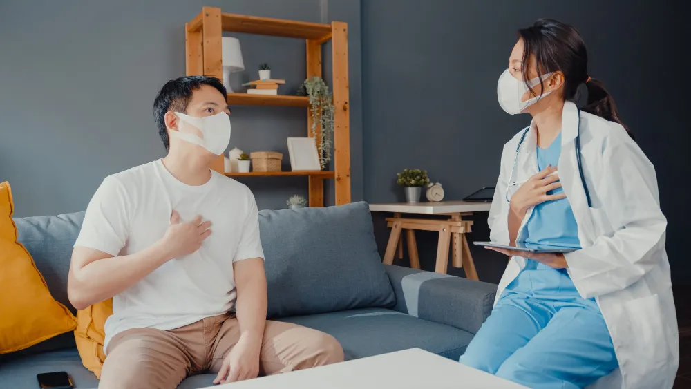 young-asia-female-physician-doctor-wear-face-mask-using-digital-tablet-sharing-good-health-test-news-with-happy-male-patient-sit-couch-house
