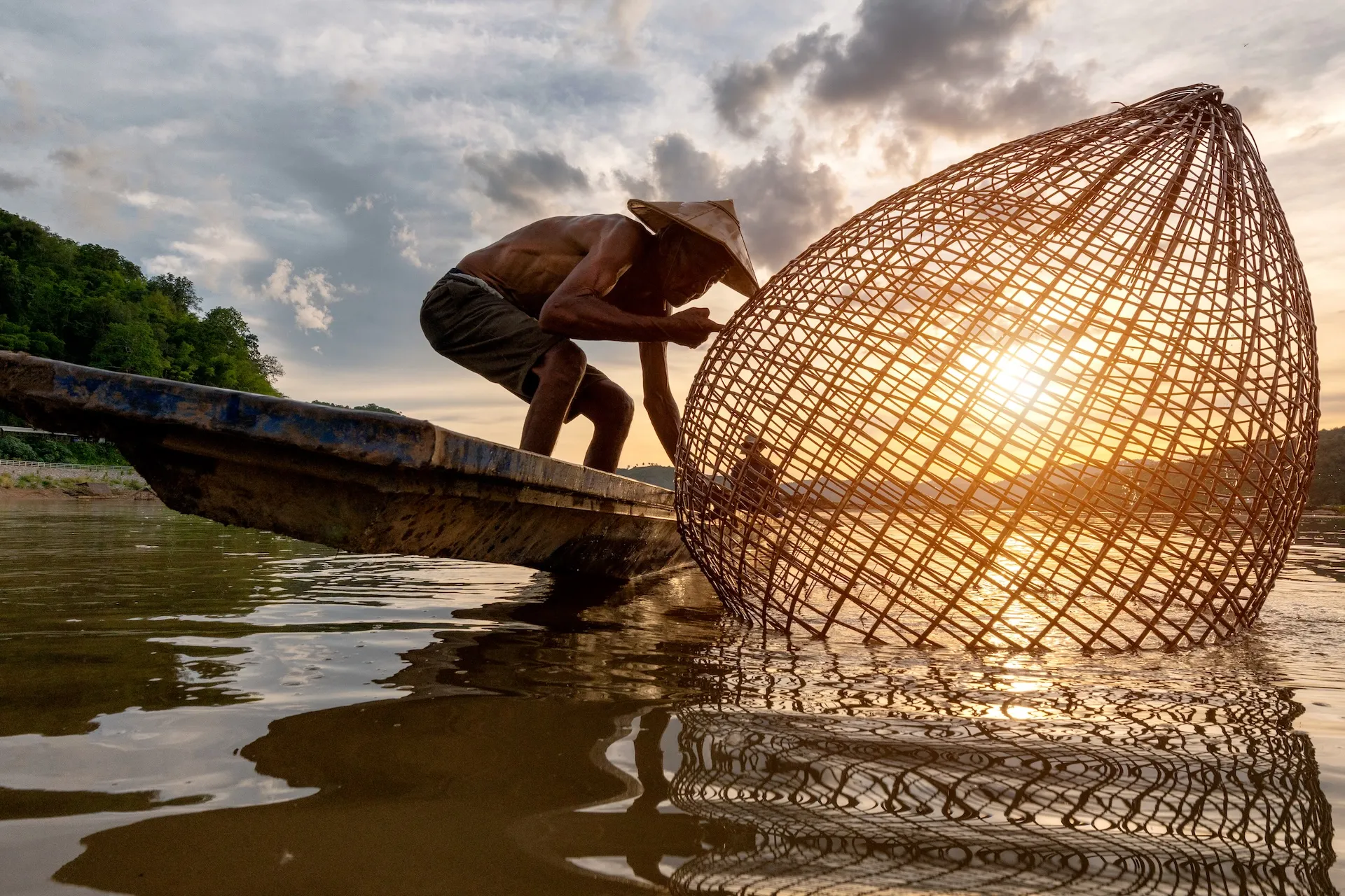 ThaifarmerlookingatfishingnetsandlookingforfishintheMekongRivershutterstock1183590049copy