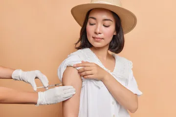 horizontal-shot-brunette-young-asian-woman-gets-inoculation-shoulder-wears-fedora-white-dress(1)